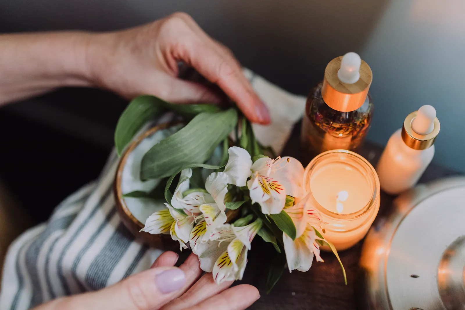 Hands arranging delicate white flowers beside a candlelit spa setting